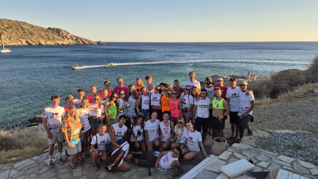 Ios Island seasonal staff group photo overlooking Mylopotas Beach, Greece, showcasing international team members working a summer season on the Greek island.