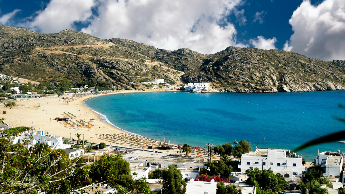 Feature-Image-mylopotas-beach-ios-greece.jpg Mylopotas Beach in Ios, Greece, overlooking the turquoise Aegean Sea and surrounding mountains on the Harmony Ios Travel Guide